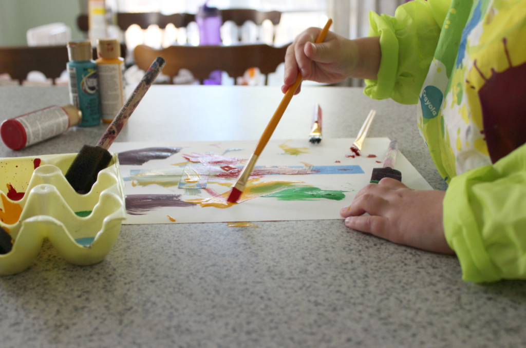 Preschooler painting with acrylic paint tape resist art craft