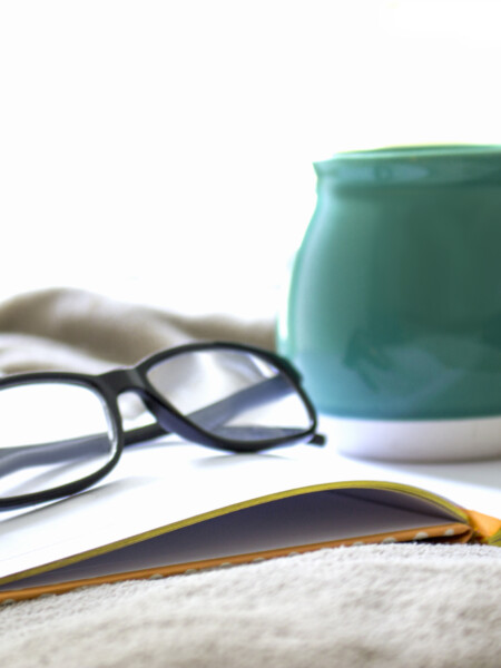 teal coffee mug and reading glasses on an open book