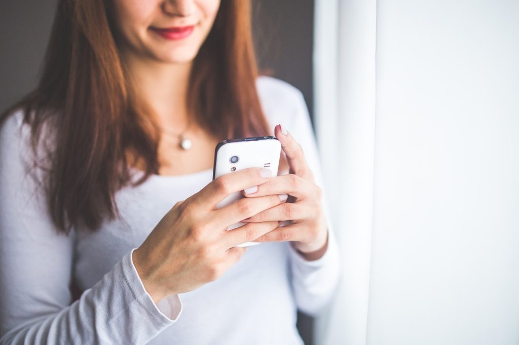 woman holding a smart phone sending a text message.  Easy ways to reconnect with your spouse after having kids