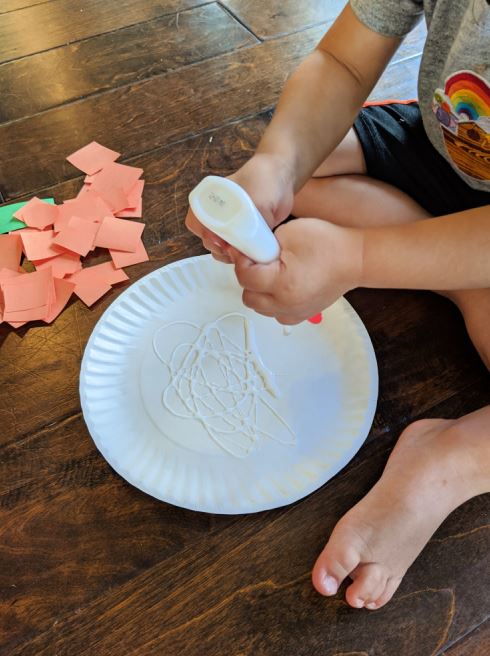 Squeezing glue onto a paper plate to make a paper plate pumpkin craft with kids