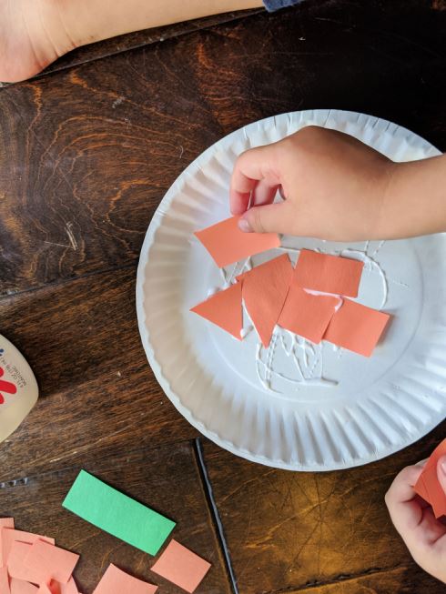 Pasting orange paper onto paper plate to make a paper plate pumpkin craft for preschoolers